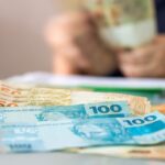 Imagem de uma mão contando cédulas de cinquenta reais e de cem reais