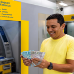 Homem sorri com dinheiro na mão em frente a caixa eletrônico do Banco do Brasil
